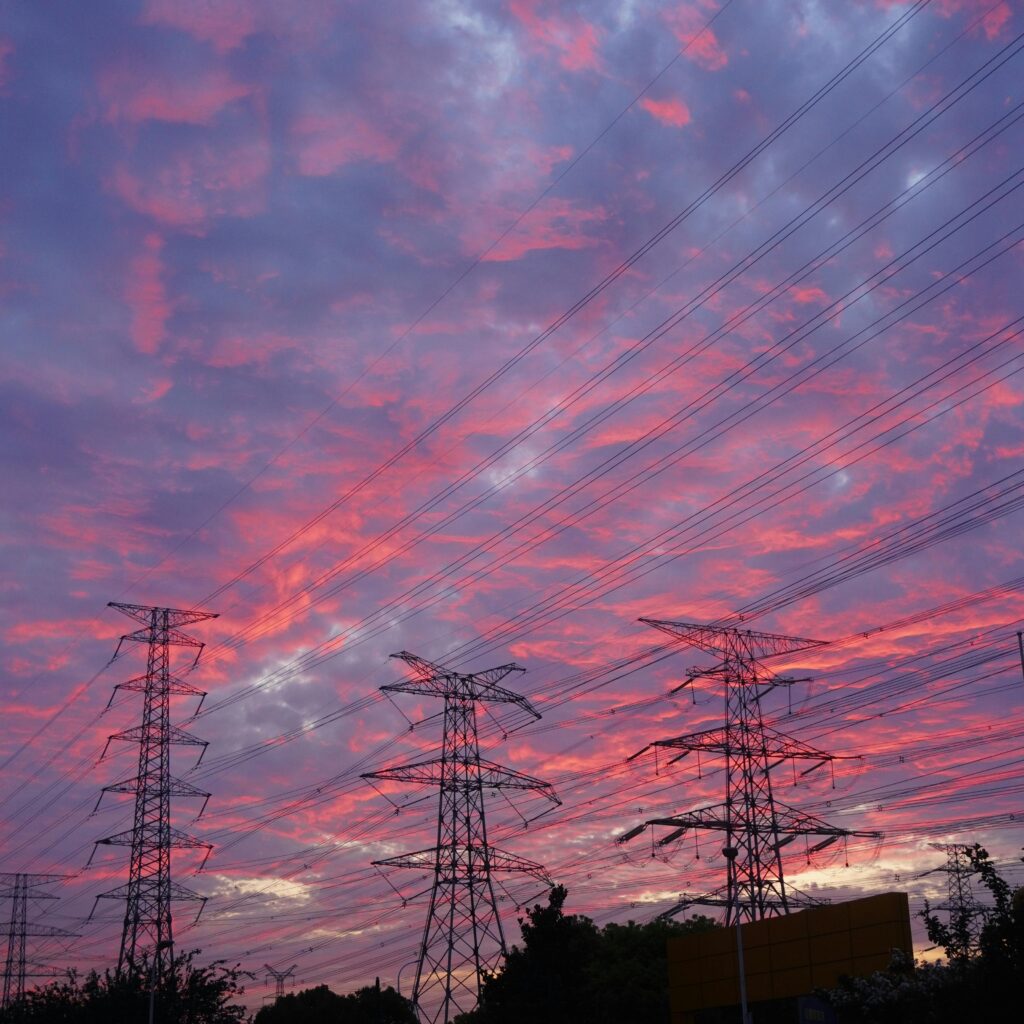 Vibrant sunset with silhouetted transmission towers and dramatic cloudscape.