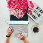 Top view of a home office workspace with laptop, coffee, flowers, and letter board.