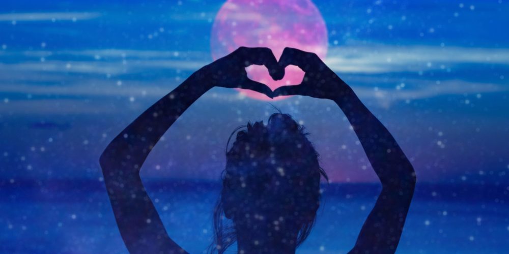 Silhouette of a girl holding heart-shape symbol for love on a starry night sky.